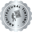 Silver circular badge with a scalloped edge labeled "ARCHITECTURAL TINTING" around the border, featuring an icon of a person applying tint to a windowpane in the center.