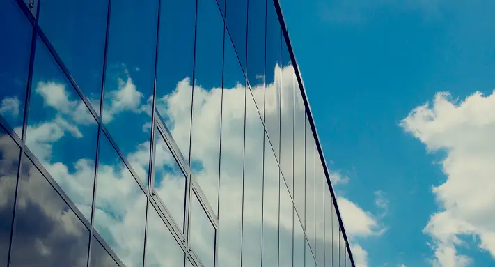 Reflection of bright blue sky and white clouds on the mirrored glass windows of a modern building.