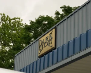 Exterior of a building with a metal facade and a sign that reads "DARK SIDE" in bold black letters against a tan background, mounted near the roofline.