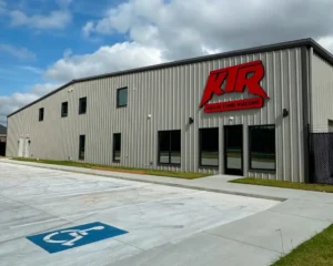 Exterior of a modern industrial building with a large red "KTR" logo and the words "Killin Time Racing" on the facade, next to a clean parking lot with a visible handicap space.