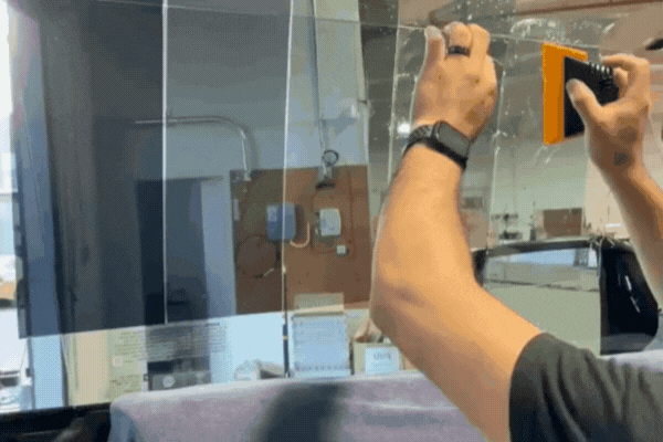 A technician applies a transparent film to a large glass window using a squeegee tool, demonstrating the process of window tinting to control light and heat. This hands-on step shows how window film is carefully smoothed onto the glass surface to improve comfort, privacy, and energy efficiency.