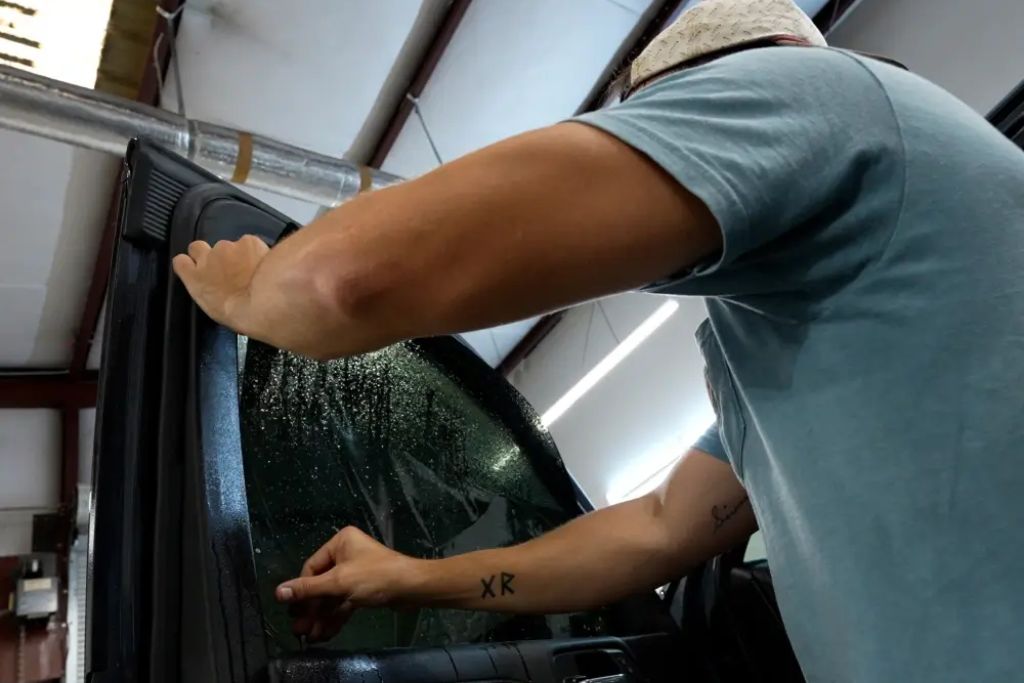 A technician installs window tint film on a vehicle door, carefully pressing the film into place on the wet glass surface. This hands-on detail highlights the skill and precision involved in professional window tinting by Dark Side Window Tinting in Augusta.