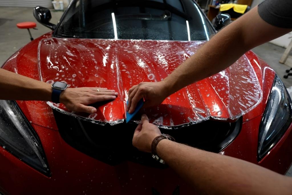 Dark Side expert applies paint protection film on the hood of a red sports car using a squeegee.