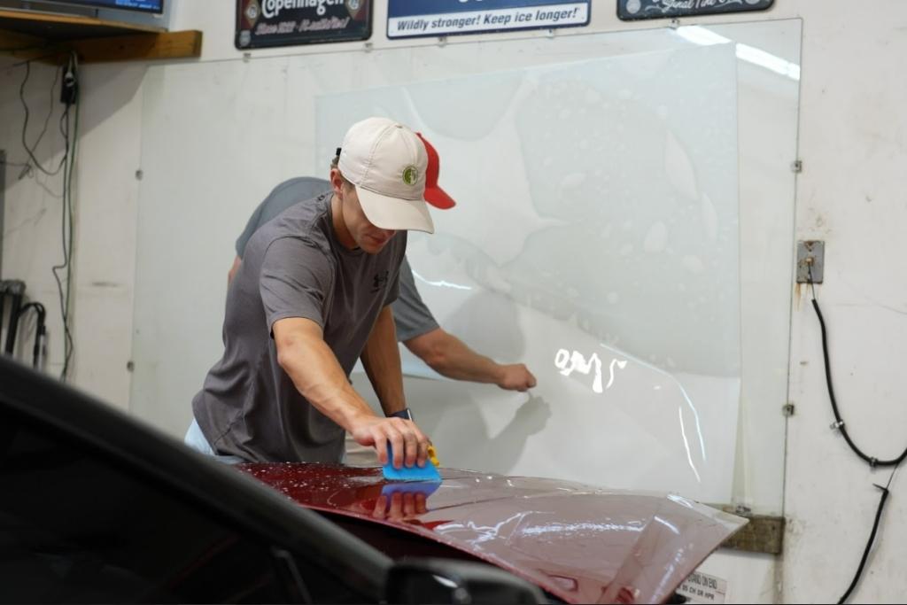 Dark Side expert installs paint protection film on the hood of a red car using a blue squeegee.
