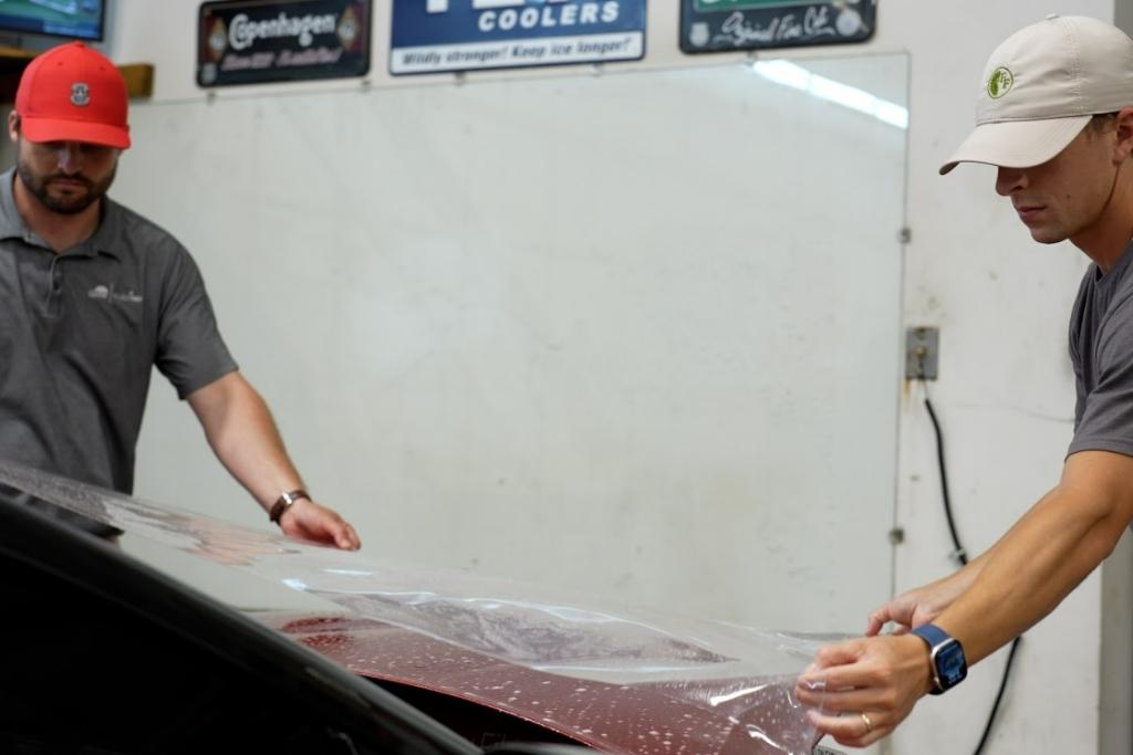 Two Dark Side experts apply paint protection film on the hood of a red car.