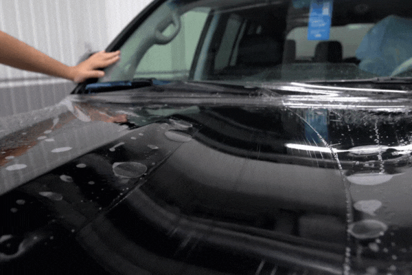 A technician applies paint protection film on the hood of a black car for a smooth and glossy finish.