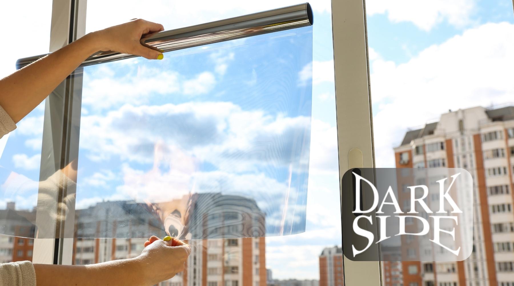 A person applying window tint film to a large glass window with a cityscape in the background.
