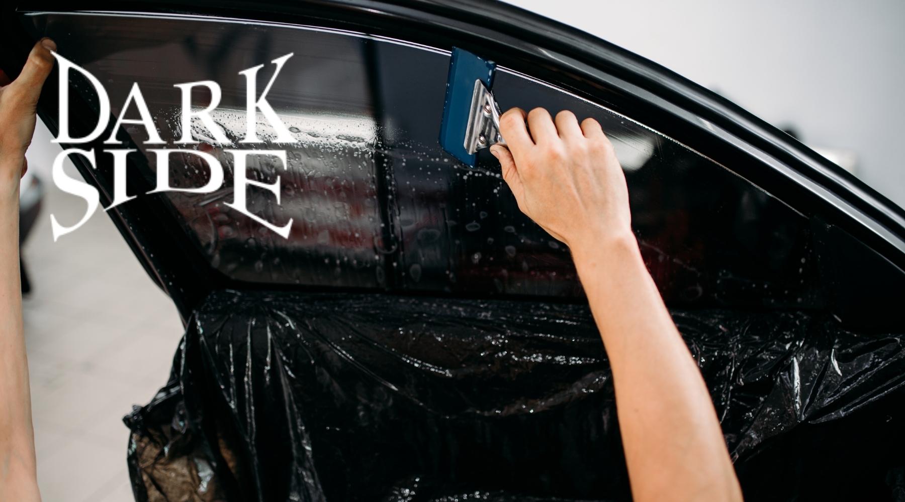 Technician installing dark window tint on a car door using a squeegee tool.