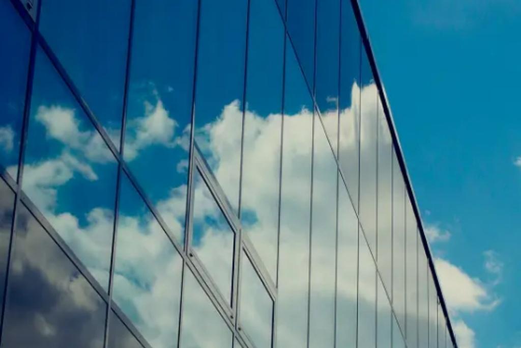 Reflective glass building with window tint showing blue sky and clouds