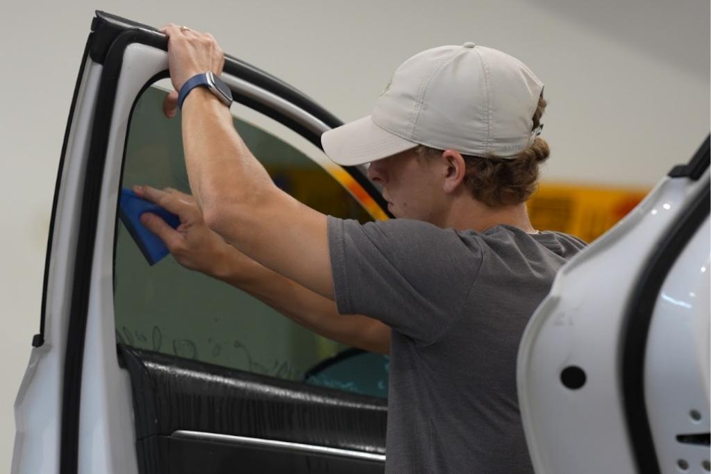 Window tint technician installing film on a vehicle door using a squeegee tool.
