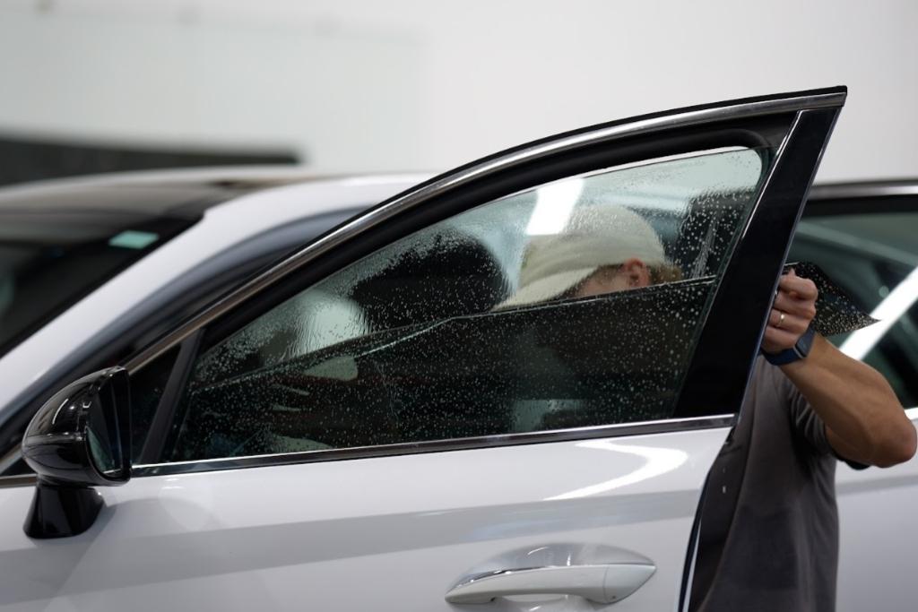 Automotive window tint installer applying film to the front door window of a white vehicle.
