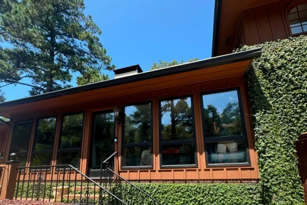 Brown house with large reflective tinted windows surrounded by greenery