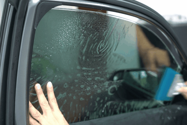 Technician applying window tint film to a car door using a squeegee tool.