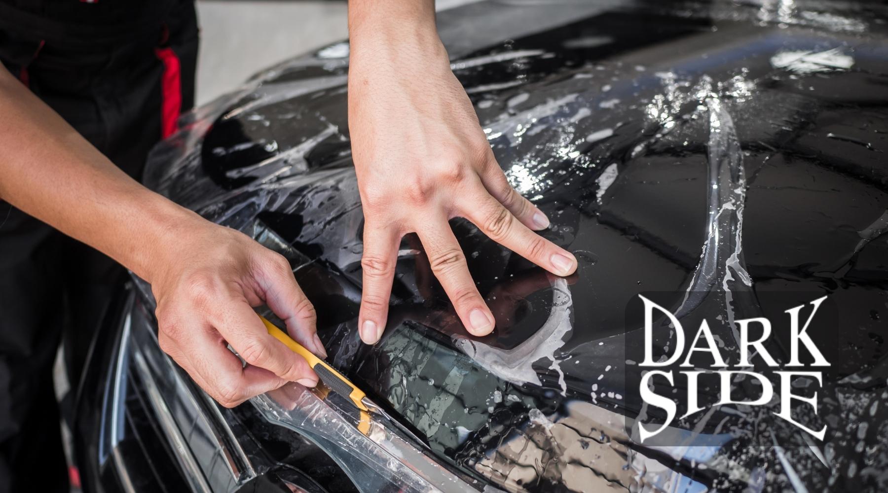 Applying paint protection film to a black car hood using a precision cutting tool.
