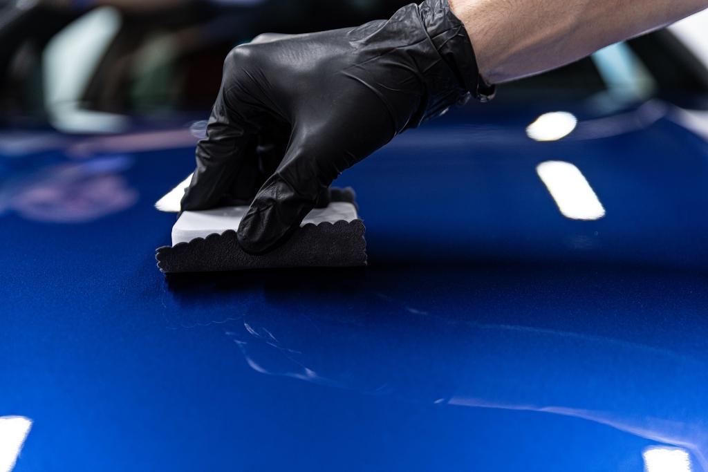 Gloved technician applying ceramic coating to the surface of a glossy blue car.