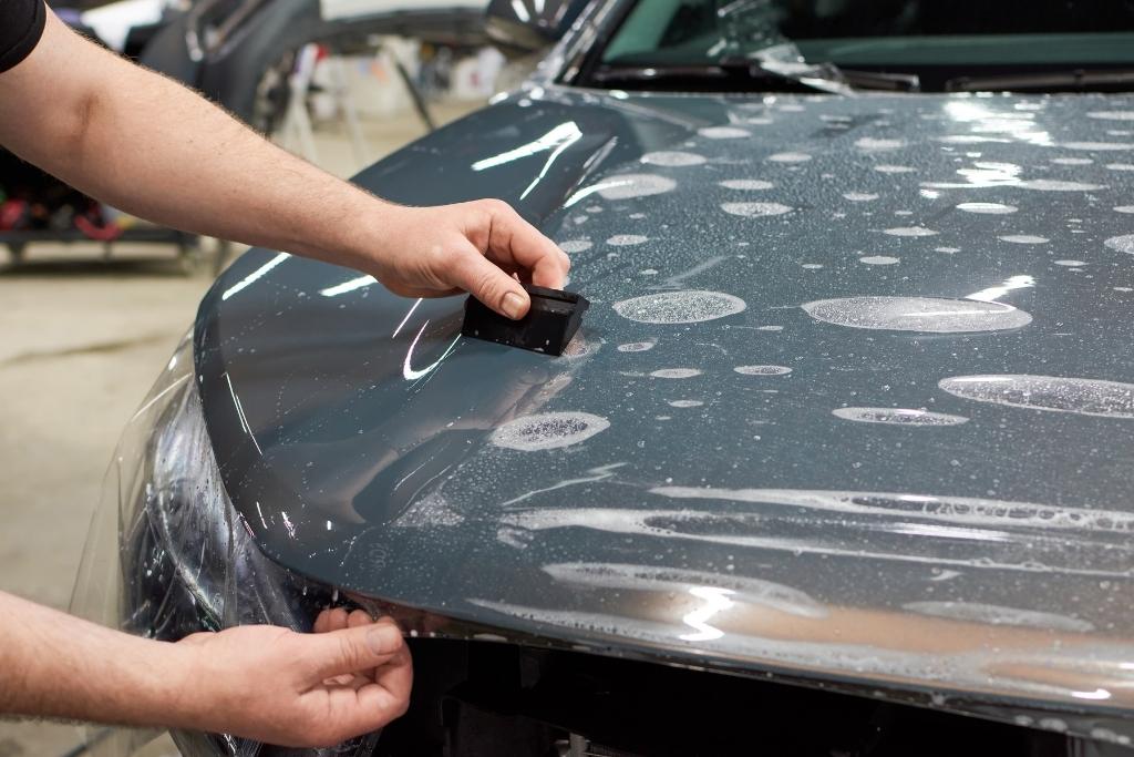 Applying paint protection film to a car hood using a squeegee tool.