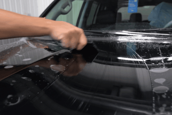 Technician smoothing paint protection film on a black car hood during professional PPF installation in Augusta, GA
