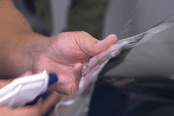 Close-up of a technician smoothing out paint protection film on a vehicle’s body panel.