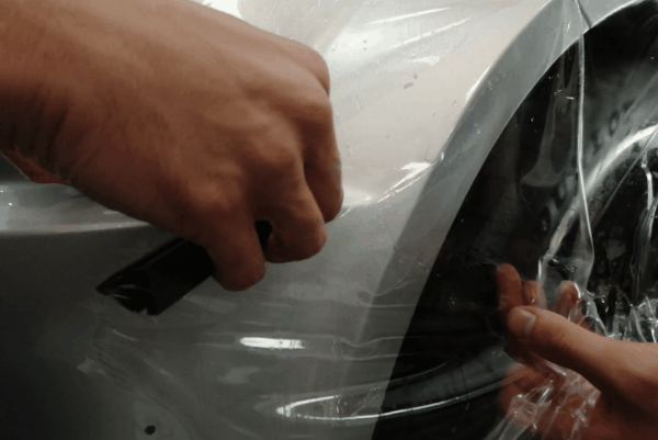 Close-up of a technician smoothing clear paint protection film around a vehicle’s trim using a blue squeegee during installation.