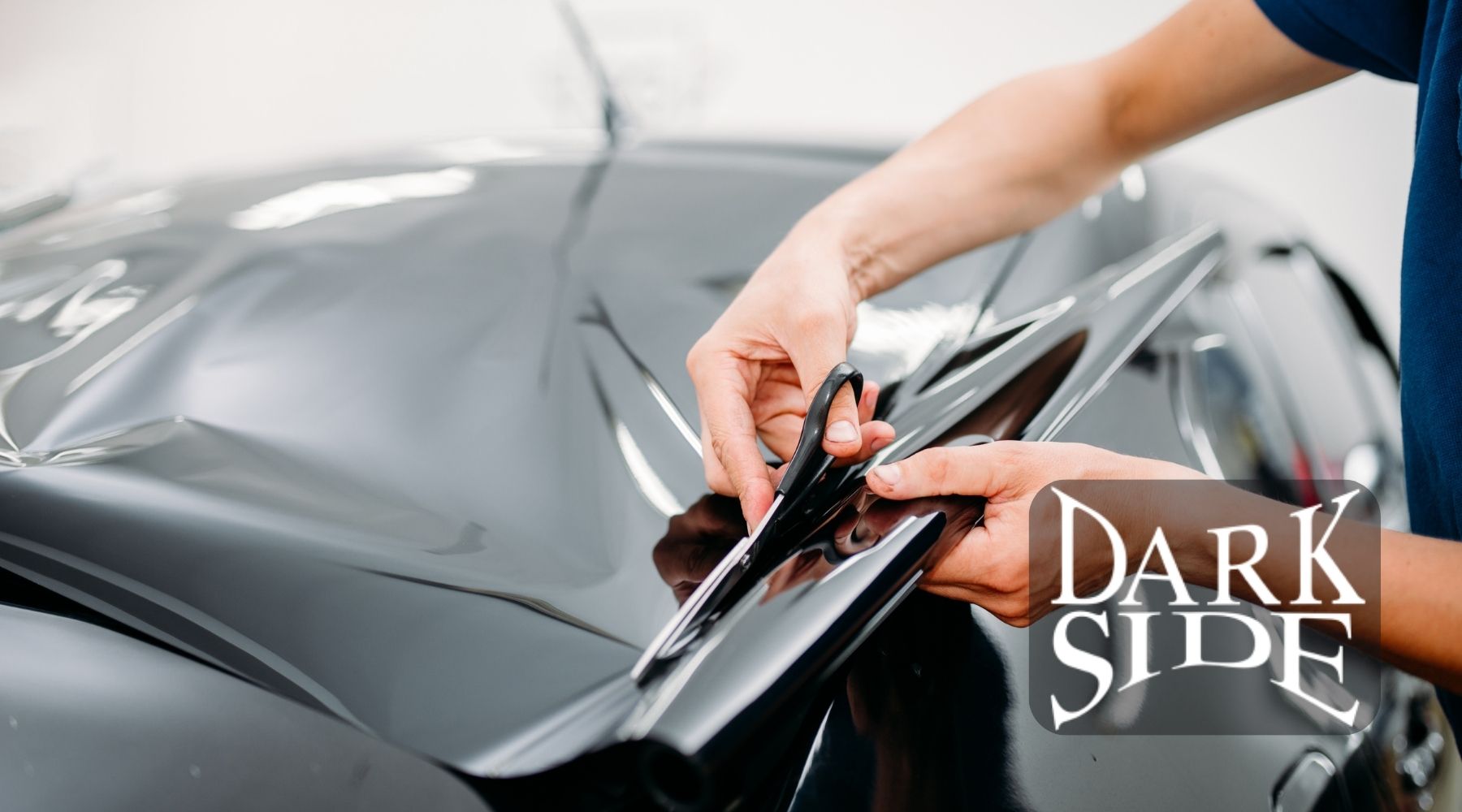 Technician cutting window tint film to fit a car window during professional installation