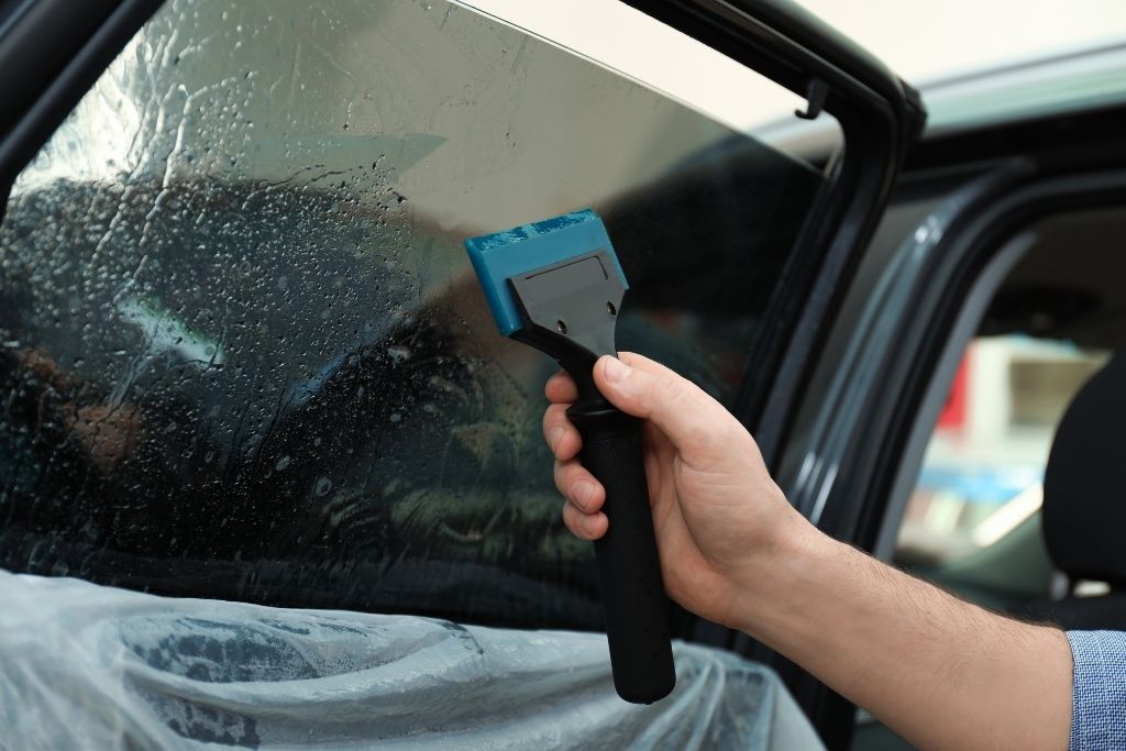 Applying car window tint with a squeegee to remove air bubbles during installation