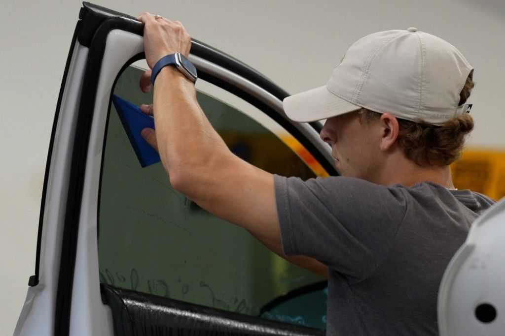 Technician applying automotive window tint film to a car door window for heat and glare protection.