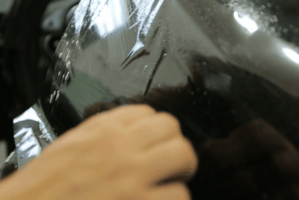 Close-up of automotive window tint film being applied to a vehicle window during professional installation.