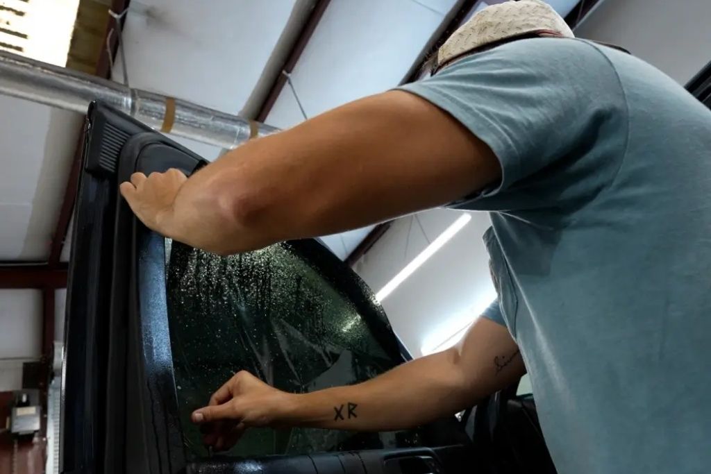 Technician applying window tint film to a vehicle side window during professional installation.