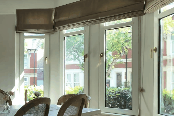 Bright dining area with large residential windows, Roman shades, and a clear view of trees and neighboring homes.