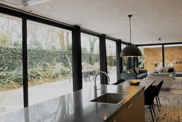 Modern kitchen and living area with floor-to-ceiling windows overlooking a bright patio and landscaped yard.