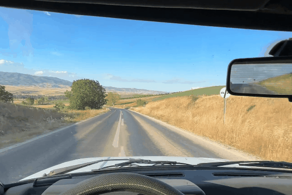 Driver’s view through a tinted windshield on a sunny rural road, showing reduced glare and clear visibility.