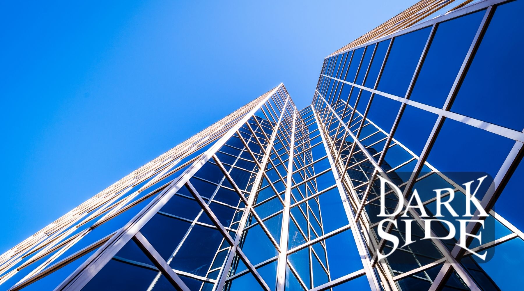 Modern commercial building with blue-tinted glass windows under a clear sky and the Dark Side Window Tinting logo.