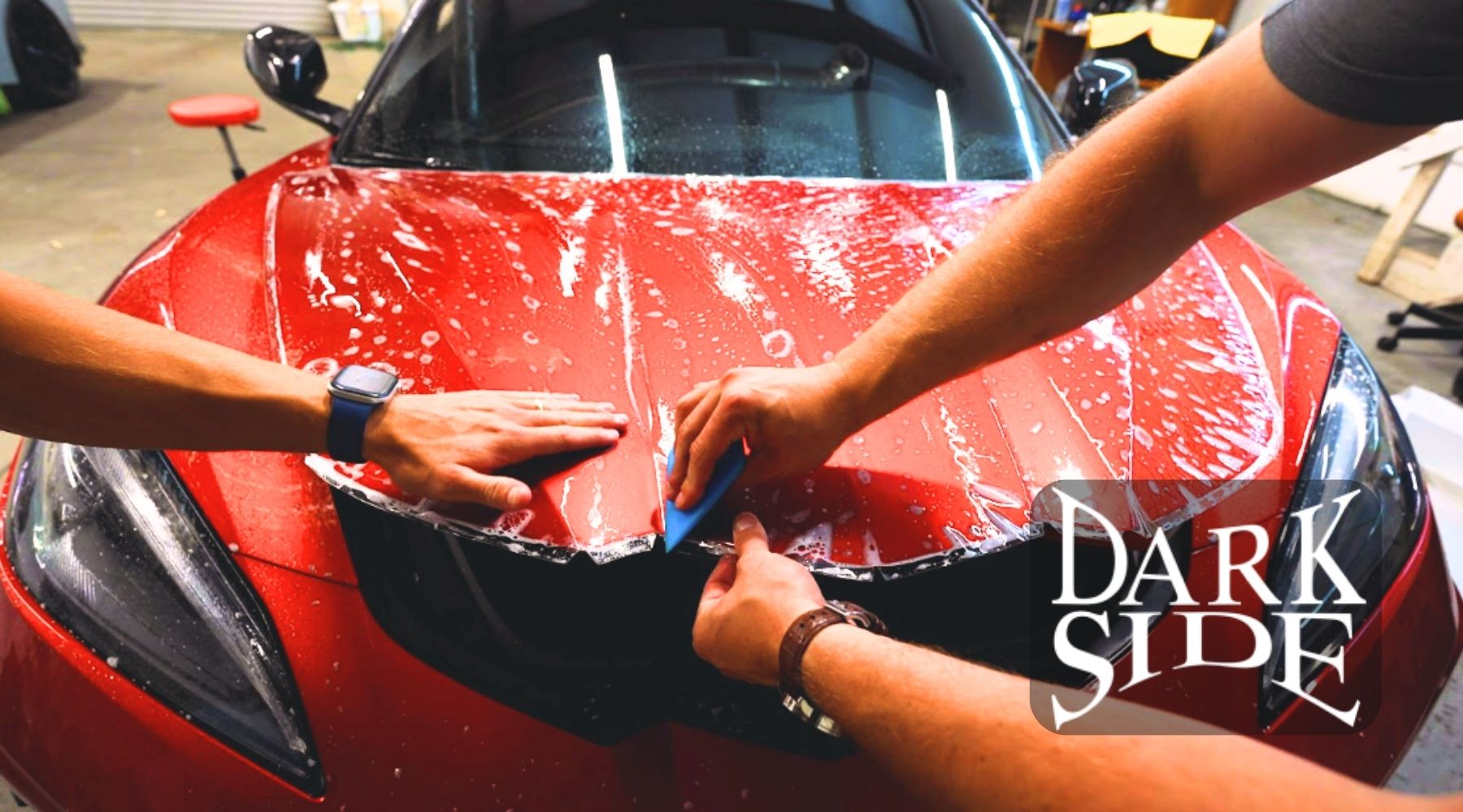 Technicians installing paint protection film on the hood of a red car at Dark Side Window Tinting