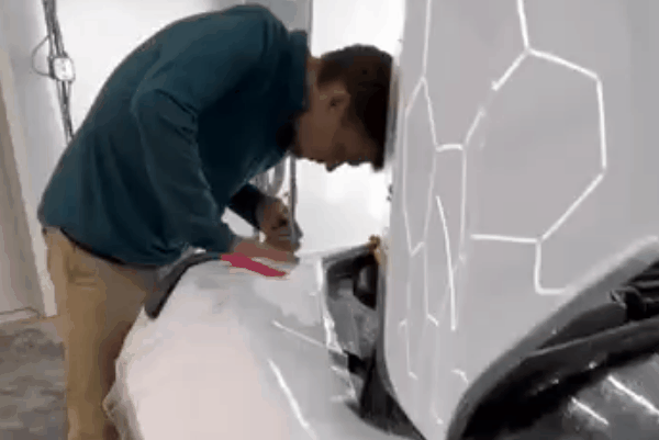 Technician applying paint protection film around the front fender and headlight area of a white vehicle
