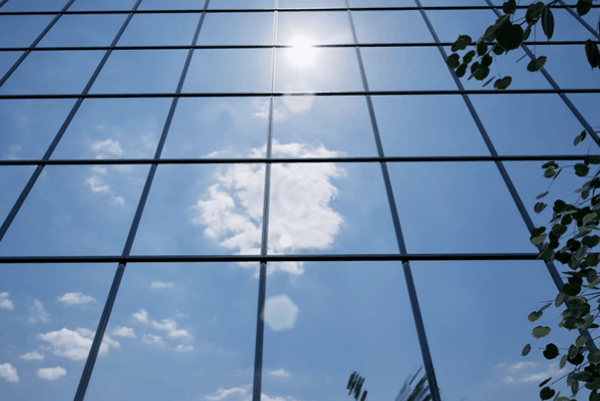 Sunlight reflecting off a modern commercial glass façade with blue sky and clouds.