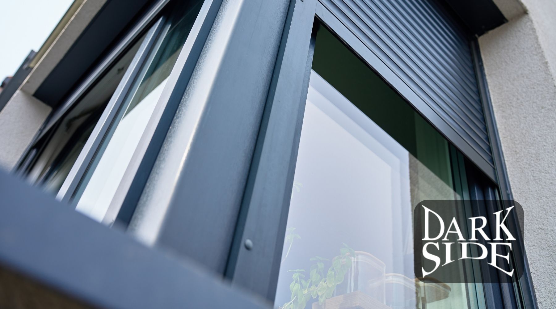 Close-up of a modern home window with a partially lowered exterior shutter and Dark Side Window Tinting logo.