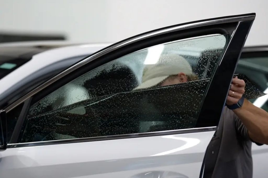 Technician installing window tint film on the side window of a white vehicle.