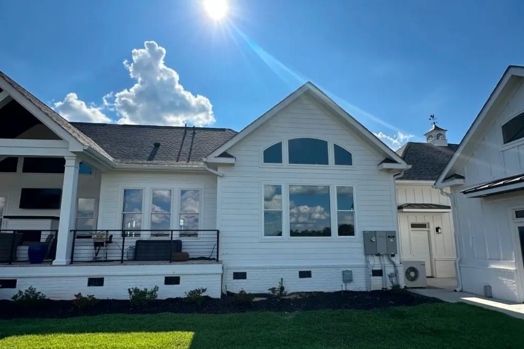 Exterior of a white home with large dark-tinted windows under bright sunlight and a clear blue sky.