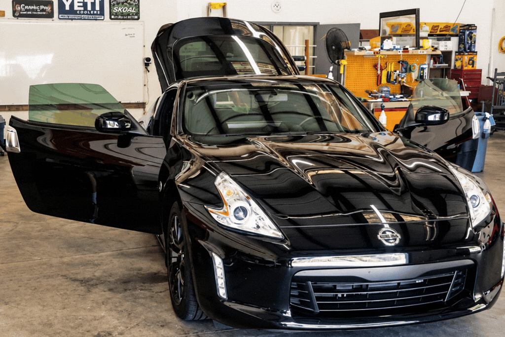 Black sports car inside an automotive tint shop during professional window tint installation.