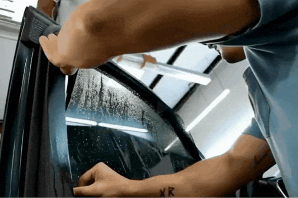 Technician applying automotive window tint film to a vehicle side window during installation.