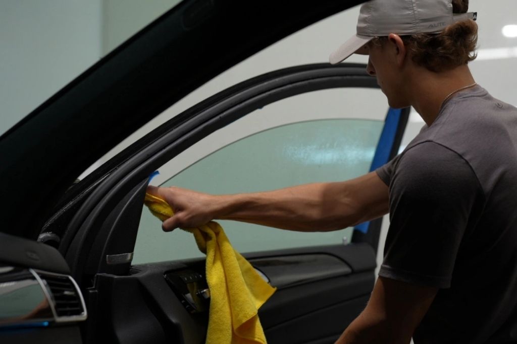 Technician cleaning a vehicle side window before professional window tint installation.